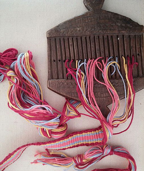 Échantillon de tissage en cours sur un métier à tisser à peigne rigide. Le peigne est taillé dans une planche de bois massif. Lisse rigide sur métier à tisser à sangle arrière, non tendue. Agrandissement : Tisserands algériens sur métier à main, carte postale, début XXe siècle.